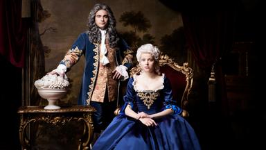 Ein Mann steht neben einer sitzenden Frau in blauer Robe.