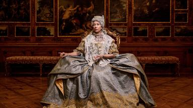 Das Bild zeigt eine Frau in historischer Kleidung, die auf einem prächtigen Stuhl sitzt. Sie trägt ein aufwändig gestaltetes Kleid, das in Grautönen gehalten ist und mit goldenen Stickereien verziert ist. Ihr Oberteil ist mit einem weißen Spitzenmantel bedeckt. Die Frau hat eine aufwändige Frisur und Schmuck angelegt, der ihren Hals und ihre Schultern ziert.  Im Hintergrund sind kunstvoll gestaltete Wände mit großen Gemälden, die Szenen aus der Antike oder Mythologie darstellen. Die Wände sind aus dunklem Holz und tragen goldene Verzierungen, die den eleganten, historischen Kontext unterstreichen. Der Boden besteht aus einem auffälligen Holzparkett in einem geometrischen Muster.   Die gesamte Szenerie vermittelt einen Eindruck von Prunk und Macht, passend zu der dargestellten historischen Figur.