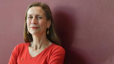 Ältere Frau mit langen Haaren blickt in die Kamera.