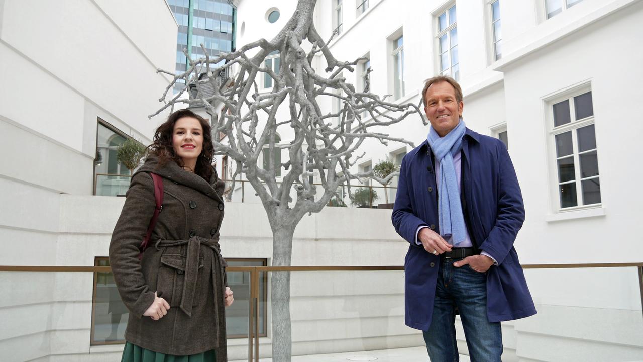 Eine Frau und ein Mann in Winterjacken vor einem skurrilen Baum im Hof des Museums.
