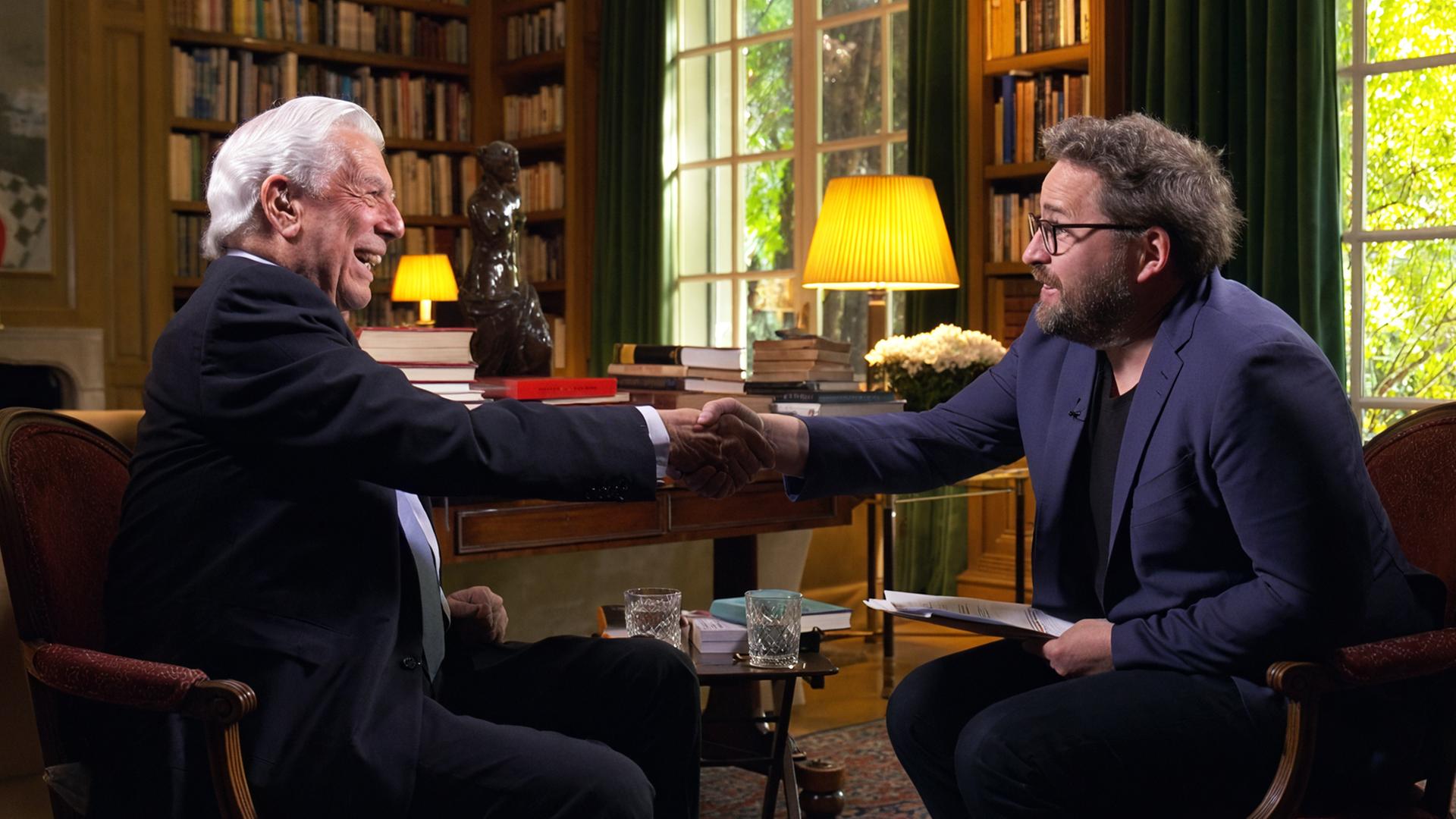 Zwei Männer, Mario Vargas Llosa und Wolfram Eilenberger, sitzen sich in einem elegant eingerichteten Raum mit Bücherregalen gegenüber und schütteln sich die Hände; sie führen ein Interview oder Gespräch in einer TV-Sendung.