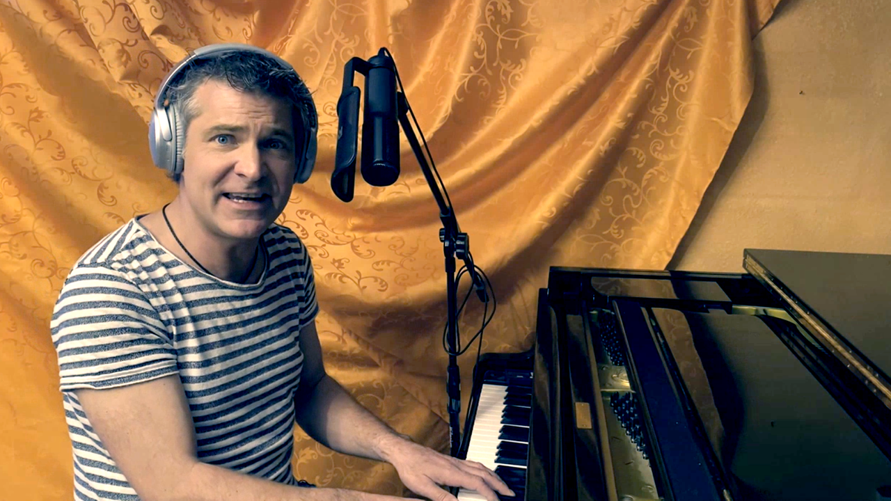 Ein Mann mit Kopfhörern singt in ein Mikrofon und spielt Klavier.