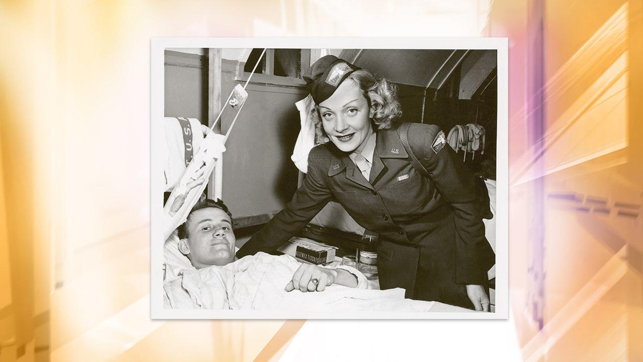 Historisches Schwarz-Weiß-Bild von Marlene Dietrich, einer Frau in Militäruniform, die sich über das Krankenbett eines Soldaten beugt.