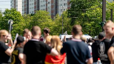 Eine Gruppe unscharf vvon hinten fotografierter Jugendlicher in schwarzen T-Shirts und mit Kurzhaarfrisuren. Ein Mädchen hat sich eine Deutschlandflagge umgebunden.