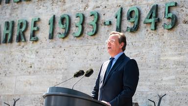 Ein Mann steht hinter einem Podest und spricht in ein Mikrofon.