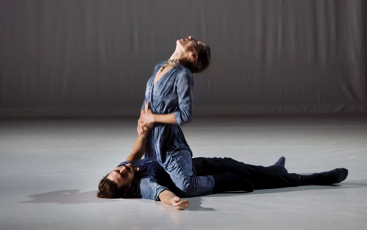 Ein Mann liegt auf dem Boden, eine Frau sitzt auf ihm, hält seinen linken Arm an ihre Brust und wirft den Kopf in den Nacken.