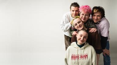 Fünf Personen stecken sprichwörtlich „die Köpfe zusammen“ – sie stehen eng beieinander und schauen in die Kamera.