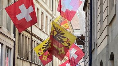 Straßenzug in Genf mit Altbauten und Schweizer Fahnen und Stadtwappen