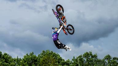 Ein Freestyle-Motocross-Fahrer macht einen Stunt und springt dabei mit seinem Motorrad in die Luft. Dabei verlässt er den Motorradsitz und schwingt das Motorrad über seinen Körper.
