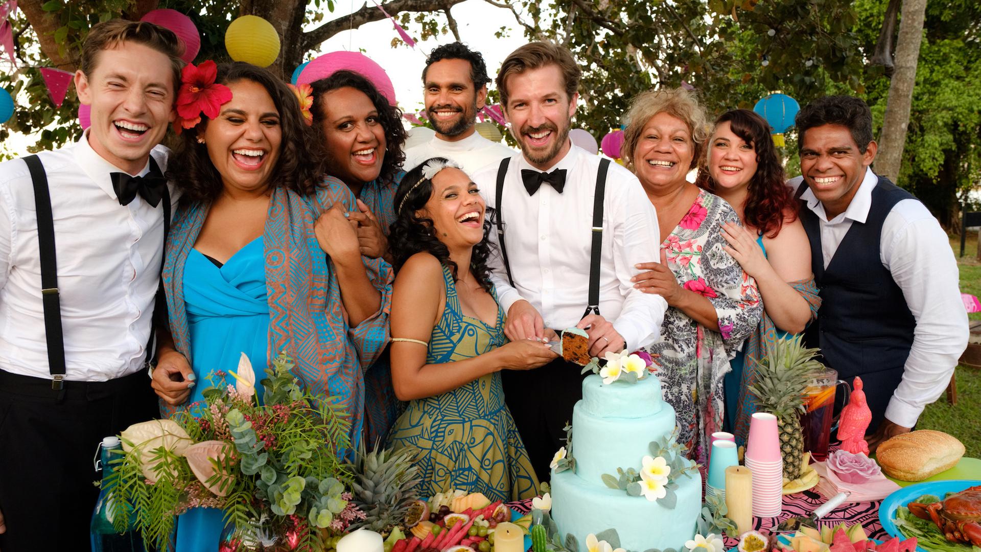 Mit dem Brautpaar Lauren (Miranda Tapsell, 3.v.l.) und Ned (Gwilym Lee, M.) freuen sich die Hochzeitsgäste: Neds Bruder Robbie (Matt Crook, l.), die Brautjungfern Dana (Elaine Crombie, l.), Kailah (Dalara Williams; 2.v.l.) und Ronelle (Shari Sebbens, r.), der Pfarrer (Rob Collins, Mitte hinten), Cousin Braydon (Shaka Cook, r.) und Tante Bree (Tessa Rose, 2.v.r.).