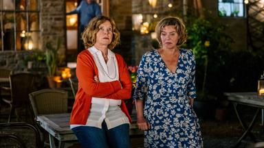 Zwei Frauen lehnen nebeneinander an einem Gartentisch.