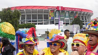 Vor dem Fußballstadion in Mexiko City stehen wie zum Karneval bunt gekleidete Männer mit Sonnebrillen und großen aufgeputzen Hüten.