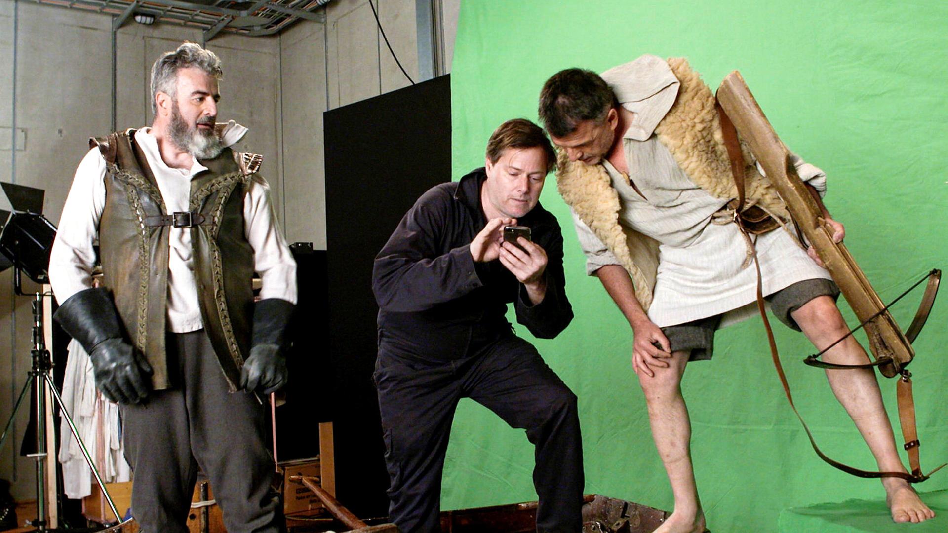 Zwei Darsteller mit dem erklärenden Regisseur bei einer Theaterprobe.