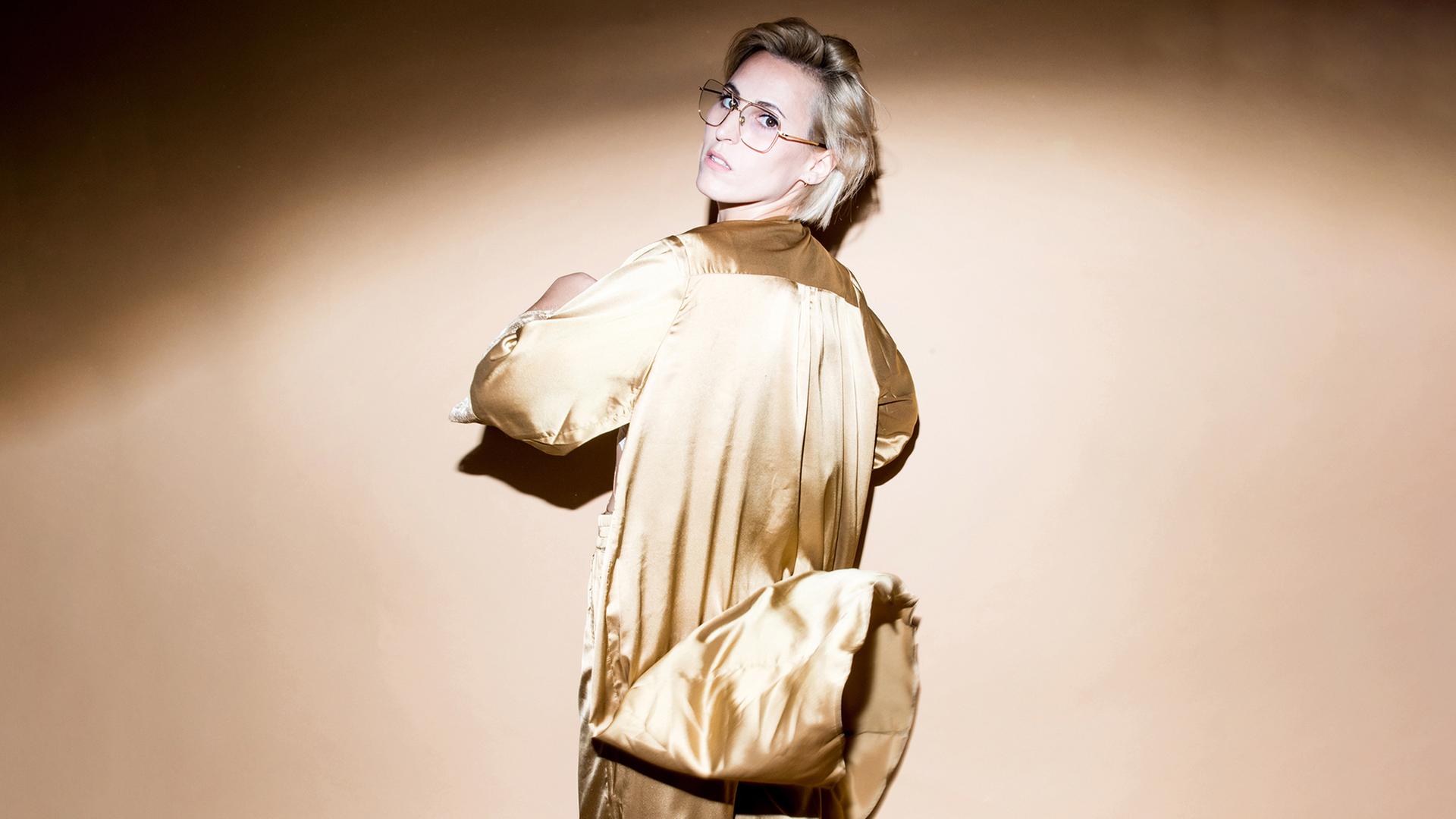 Eine blonde Frau mit Brille und goldenem Outfit