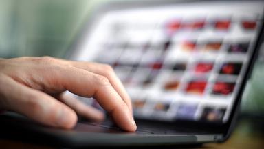 Die Finger einer Hand auf dem Tastatur eines geöffneten Laptops.