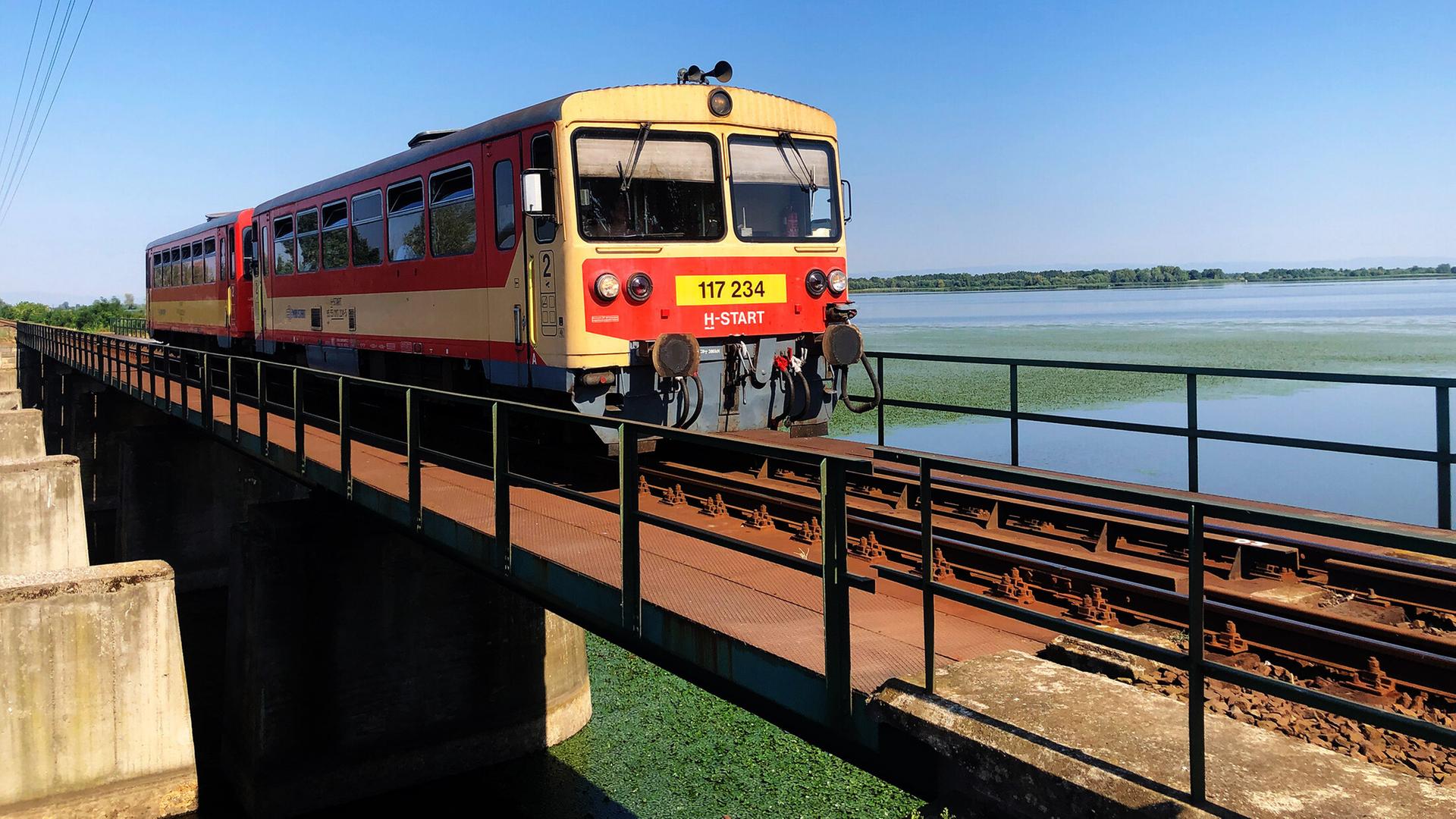 Ein Zug fährt über eine Bahnbrücke über einen Stausee.