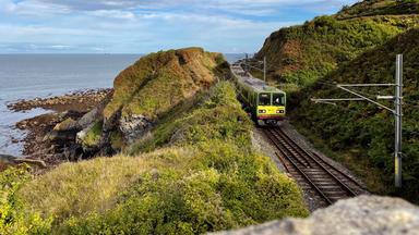Ein Zug fährt an einer grünen Küste entlang.