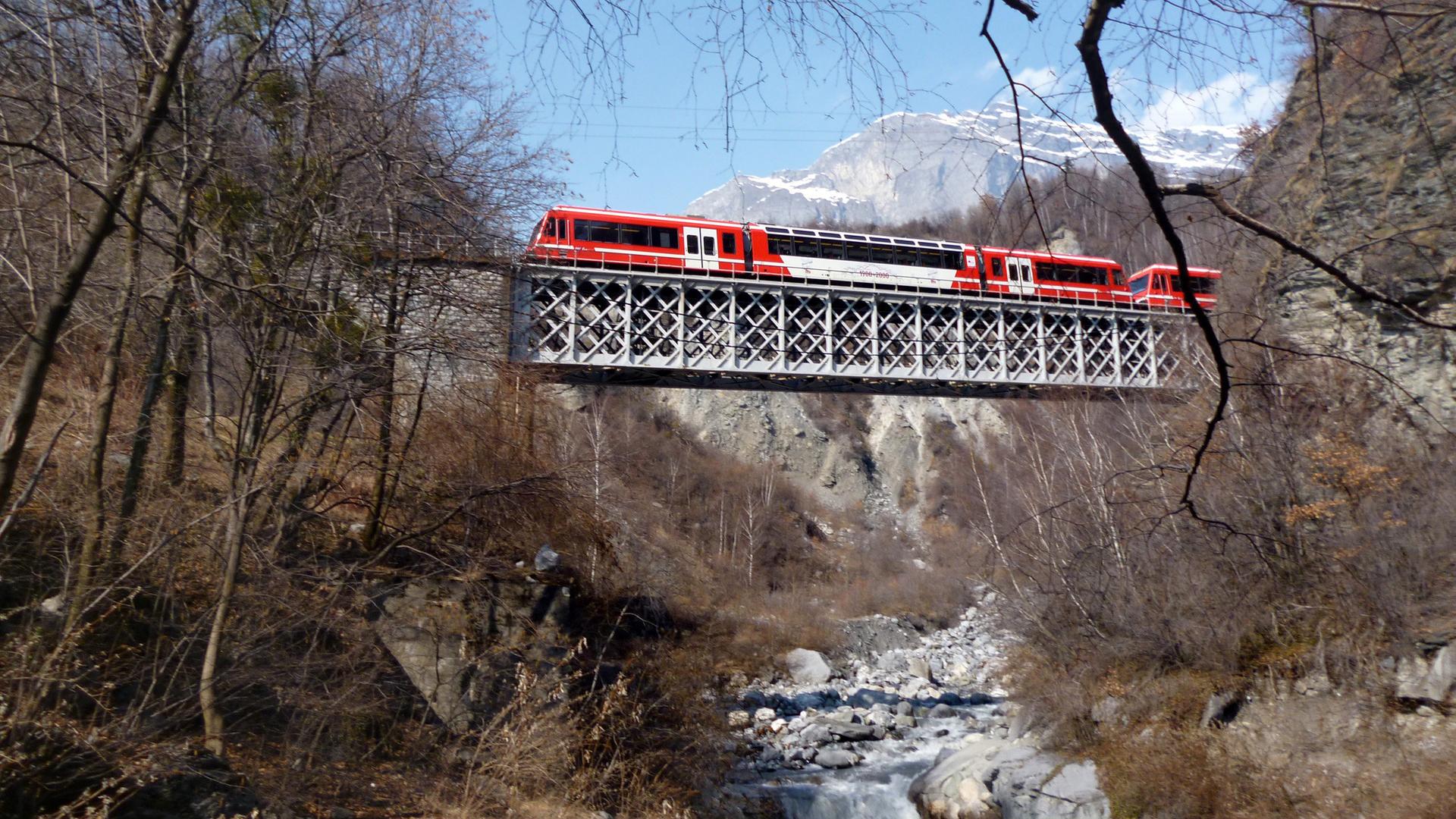Ein Zug fährt über eine Metallbrücke über einen Gebirgsbach.