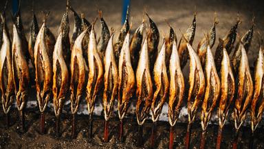 Steckerlfische auf Holzstöcken im Sand.