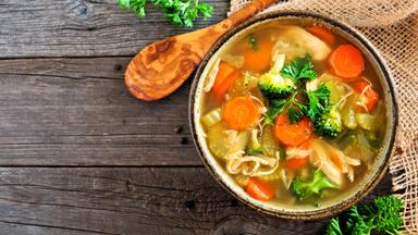 Hausgemachte Hühnersuppe mit Gemüse, Ansicht von oben mit Freiraum auf rustikalem Holzhintergrund.