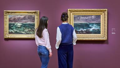 Zwei Personen sehen sich Gemälde von Meereswellen an.