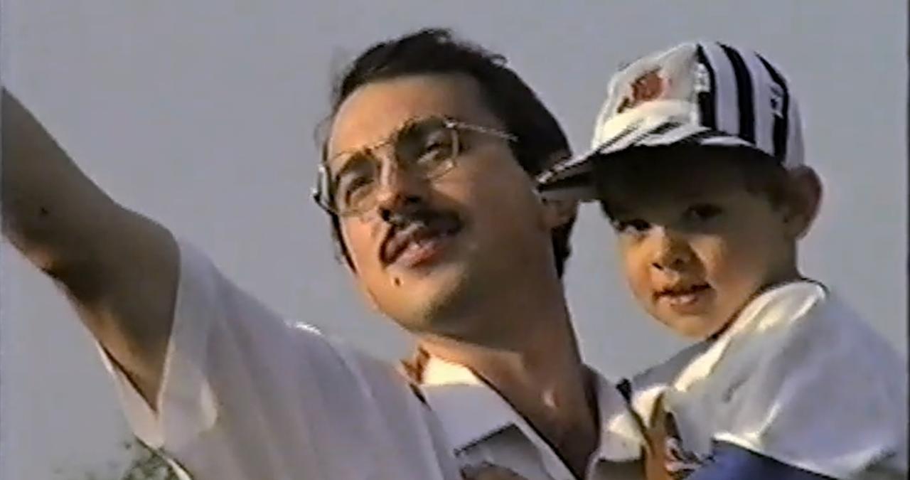 Mann mit Kind auf Arm streckt einen Arm nach oben.