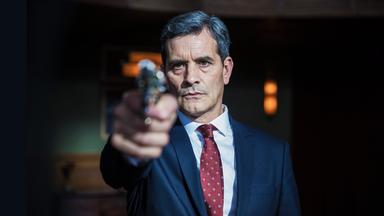 Ein Mann in einem blauen Anzug hat eine Waffe im Anschlag