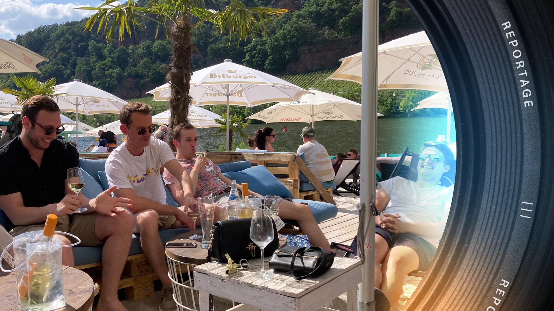 Drei junge Männer sitzen in einer Mosel-Strandbar, alle trinken Weißwein. Im Vordergrund ein transparenter Weinkühler.