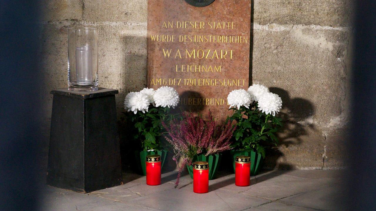 Drei Grabkerzen und weisse Blumen vor einer Gedenktafel