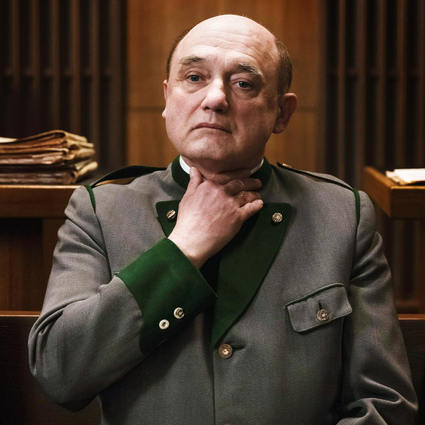 Ein Mann fasst sich mit ernstem Blick an den Hals.