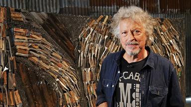 Der Musiker Wolfgang Niedecken vor einer Kunstinstalltion aus vielen Messern.