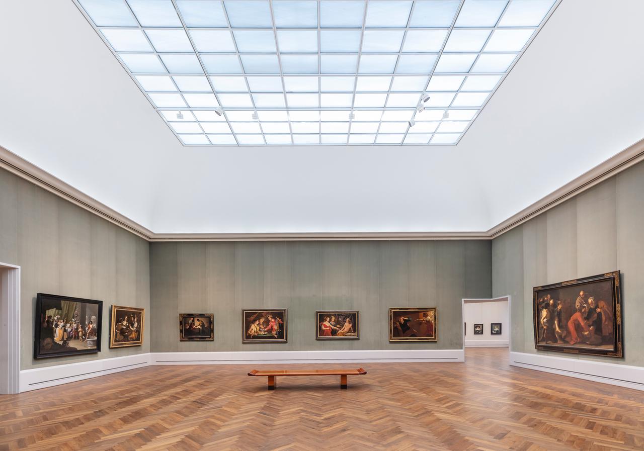 Ein großer Raum in einem Museum. An den Wänden hängen alte Gemälde.