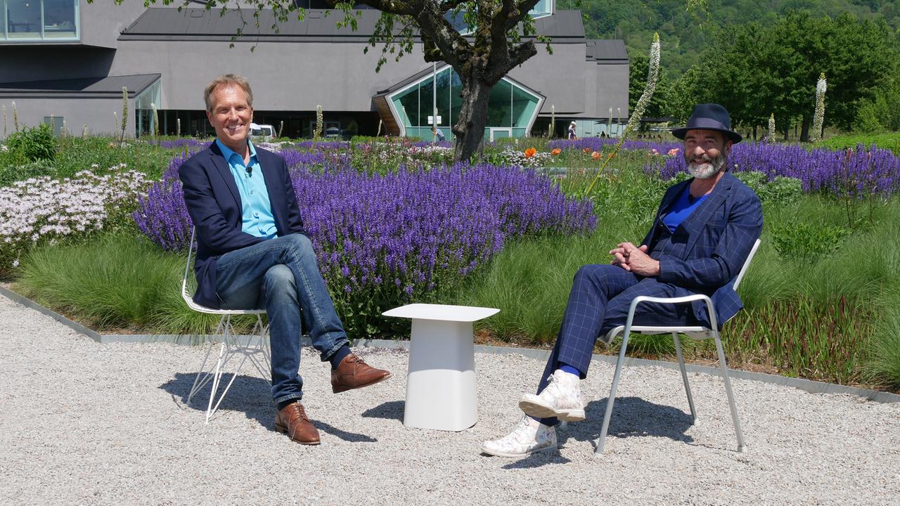 Der Moderator und der Gast im Garten auf verschiedenen Stühlen.
