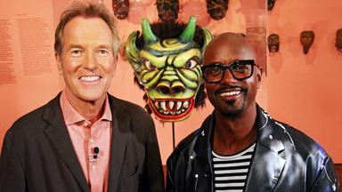 Gastgeber Markus Brock mit dem Schauspieler Yared Dibaba vor einer gruseligen grünen Maske mit Hörnern.