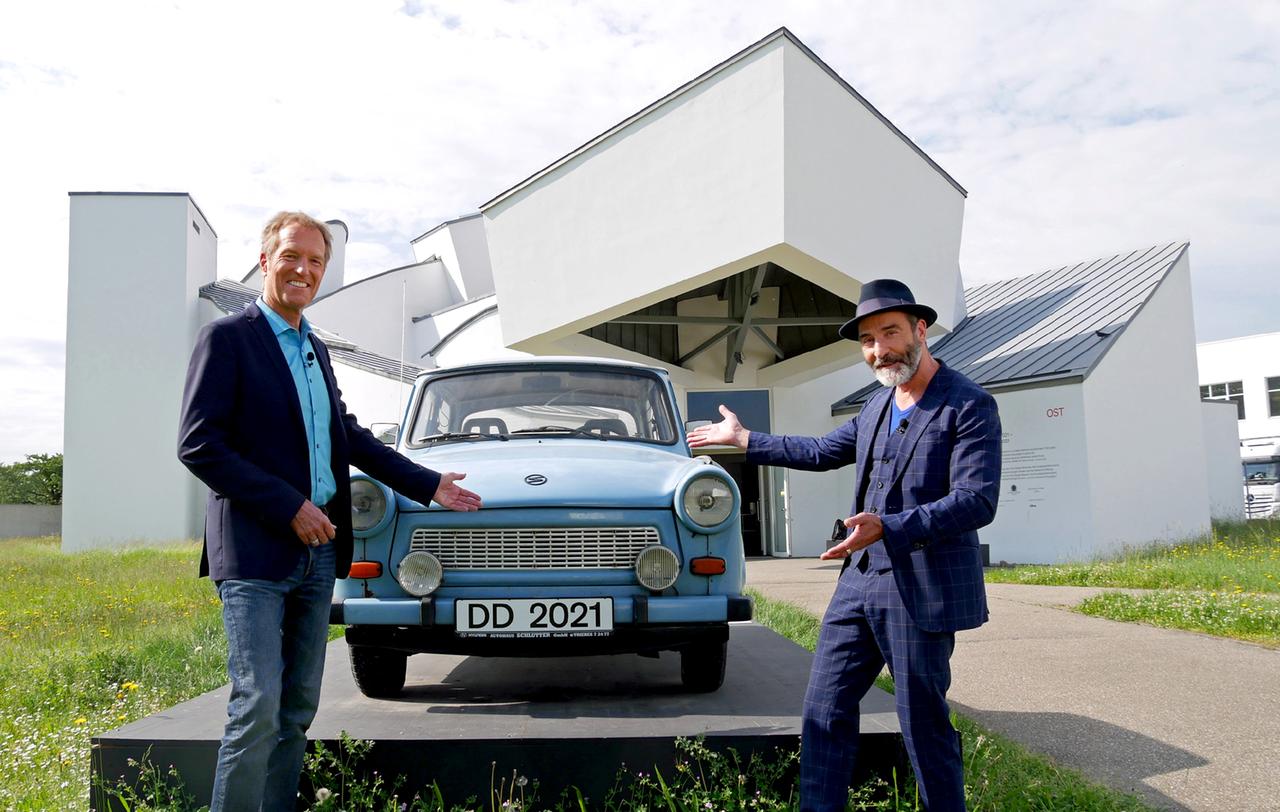 Zwei Männer und ein Trabbi vor einem architektonisch auffälligem Bau