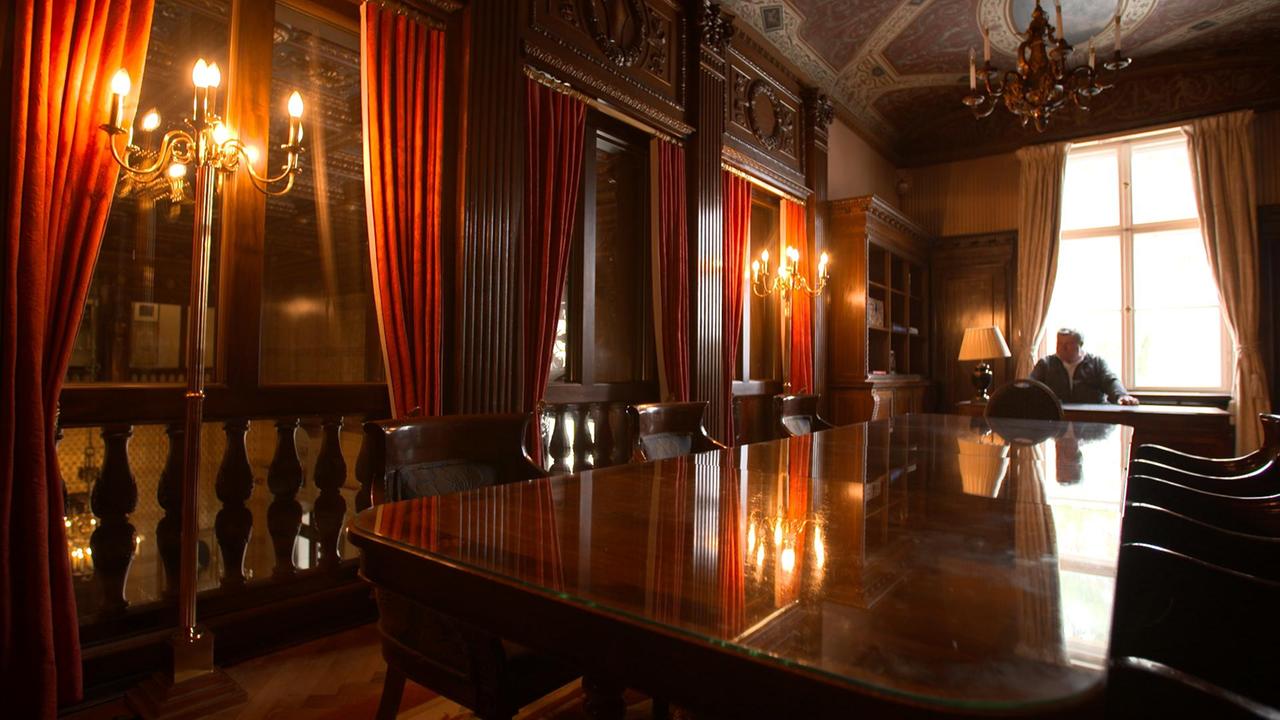 Mann an großem Tisch in Raum mit roten Samtvorhängen