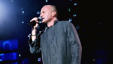 Phil Collins singt auf der Bühne in ein Mikro.