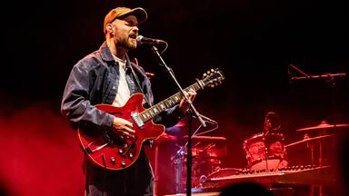 Ein Mann, der Gitarre spielt, singt in ein Mikrofon.