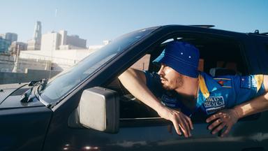 Ein Mann, der einen Hut trägt, schaut aus dem Autofenster an der Fahrerseite eines Auots.