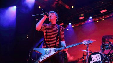 Man sieht einen Mann auf der Bühne in ein Mikrofon singen und E-Gitarre spielen.