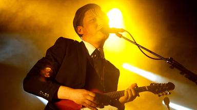 Ein Mann, der E-Gitarre spielt, singt in ein Mikrofon.