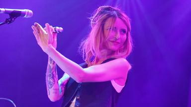 Eine Frau steht mit einem Musikinstrument in der Hand vor einem Mikrofon.