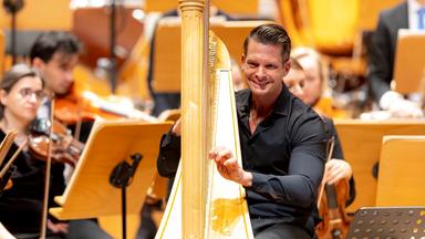 Ein Mann spielt auf einer Harfe, umgeben von einem Orchester.