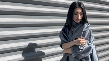 Eine Frau mit langen dunklen Haaren in einer extravaganten, blassblauen, glänzenden Bluse