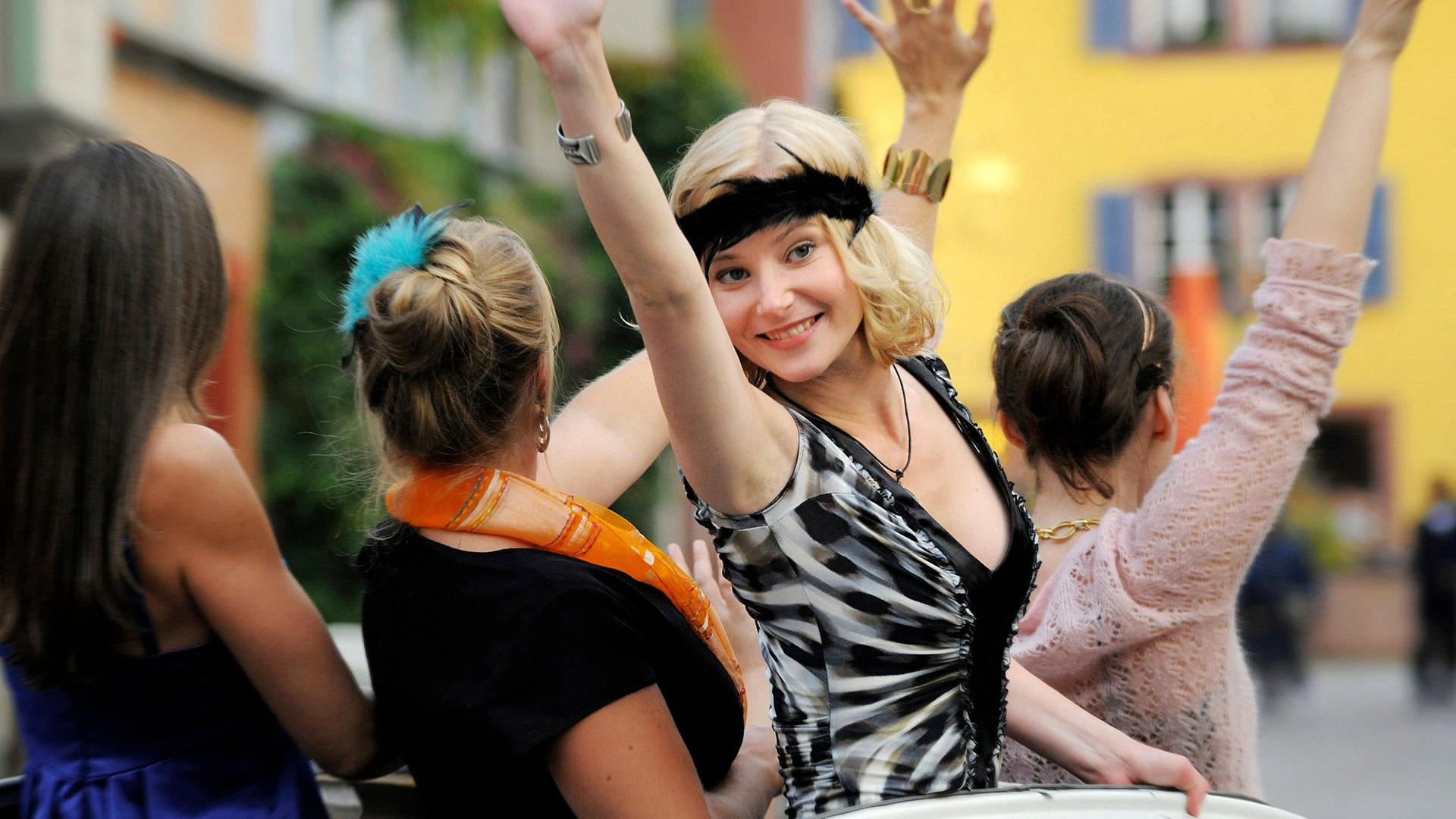 Eine Frau winkt aus einem Auto.