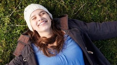 Eine junge Frau liegt auf dem Rücken im Gras.