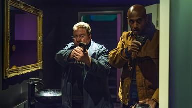 In einem Nachtclub-Badezimmer zielen Erichsen (Armin Rohde) und Elias (Tedros Teclebrhan) mit gezogenen Waffen entschlossen in Richtung eines unsichtbaren Gegners.