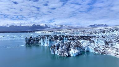 Abbruchkante am Rand einer riesigen Gletscherzunge, im Hintergrund Berge.