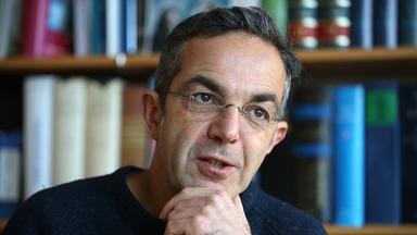 Mann mit randloser Brille vor einem Bücherregal. Portrait.