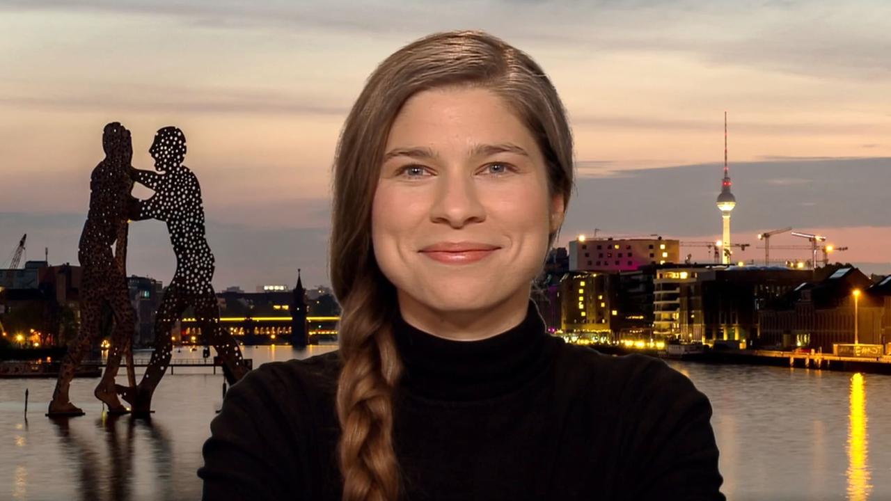 Eine junge Frau mit braunem geflochtenen Haar vor dem Hintergrund Berlins.